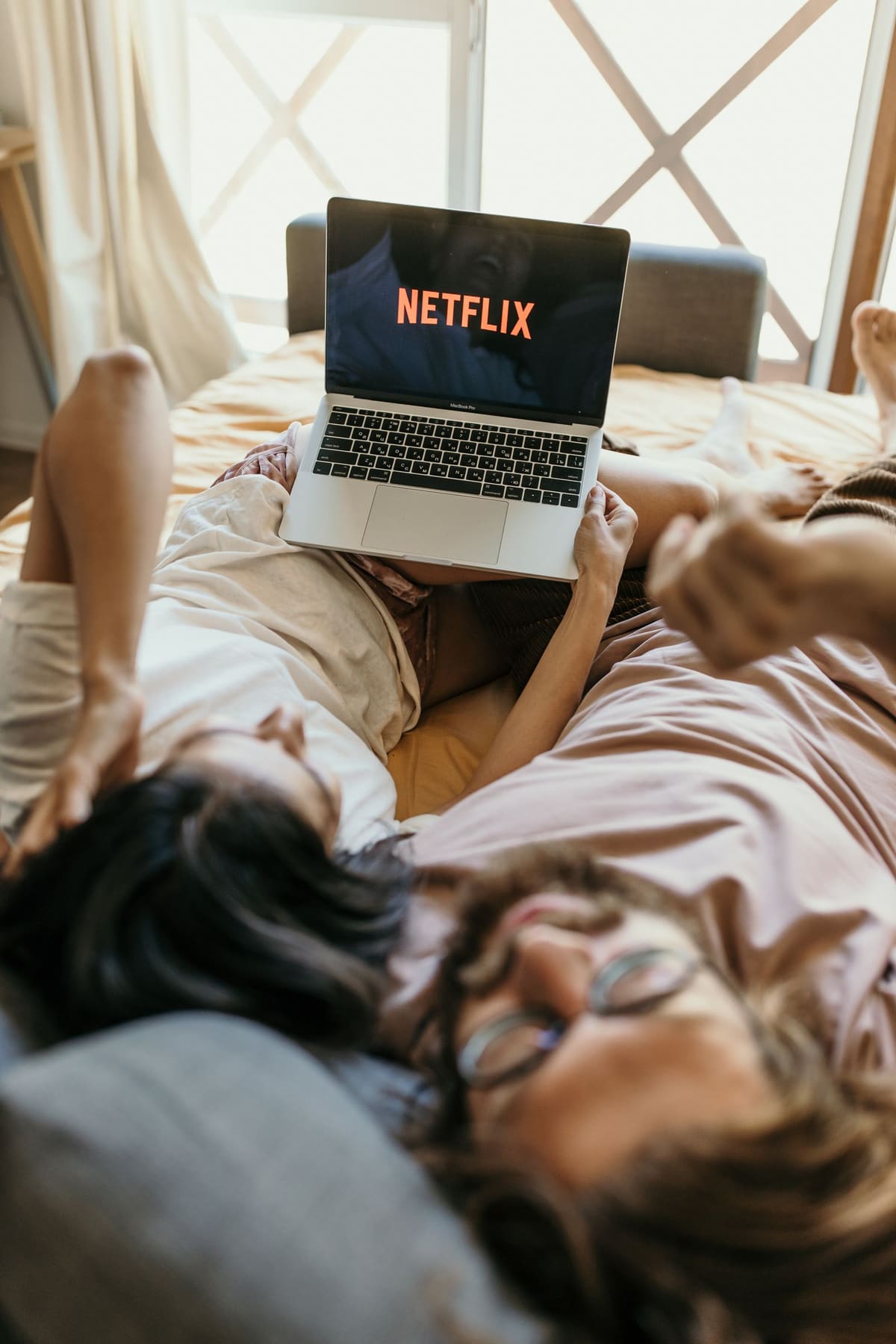 Pasangan berbaring di kasur menonton netflix di laptop