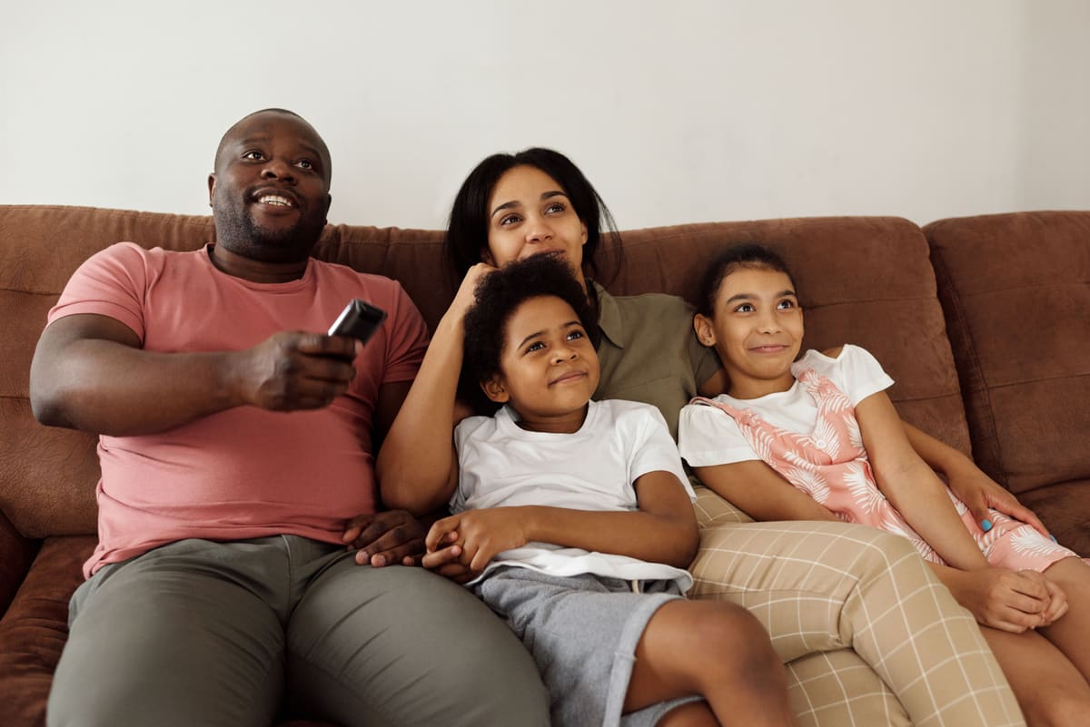 Keluarga duduk di brown sofa menonton TV