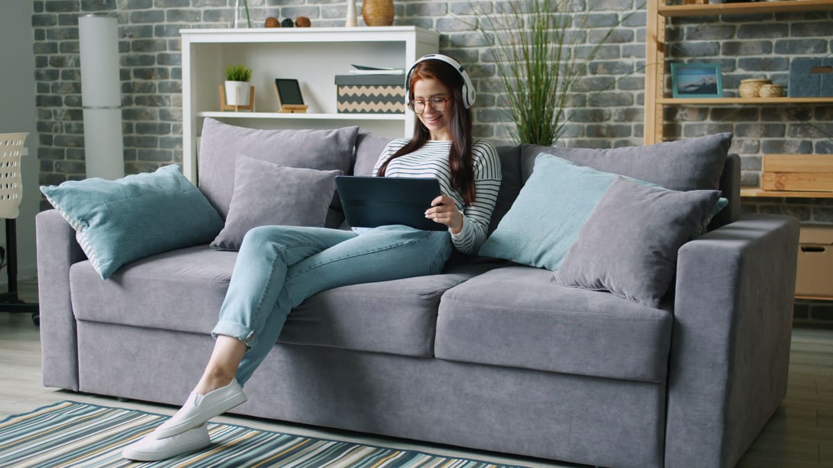 Wanita bersantai di sofa dengan tablet dan headphone