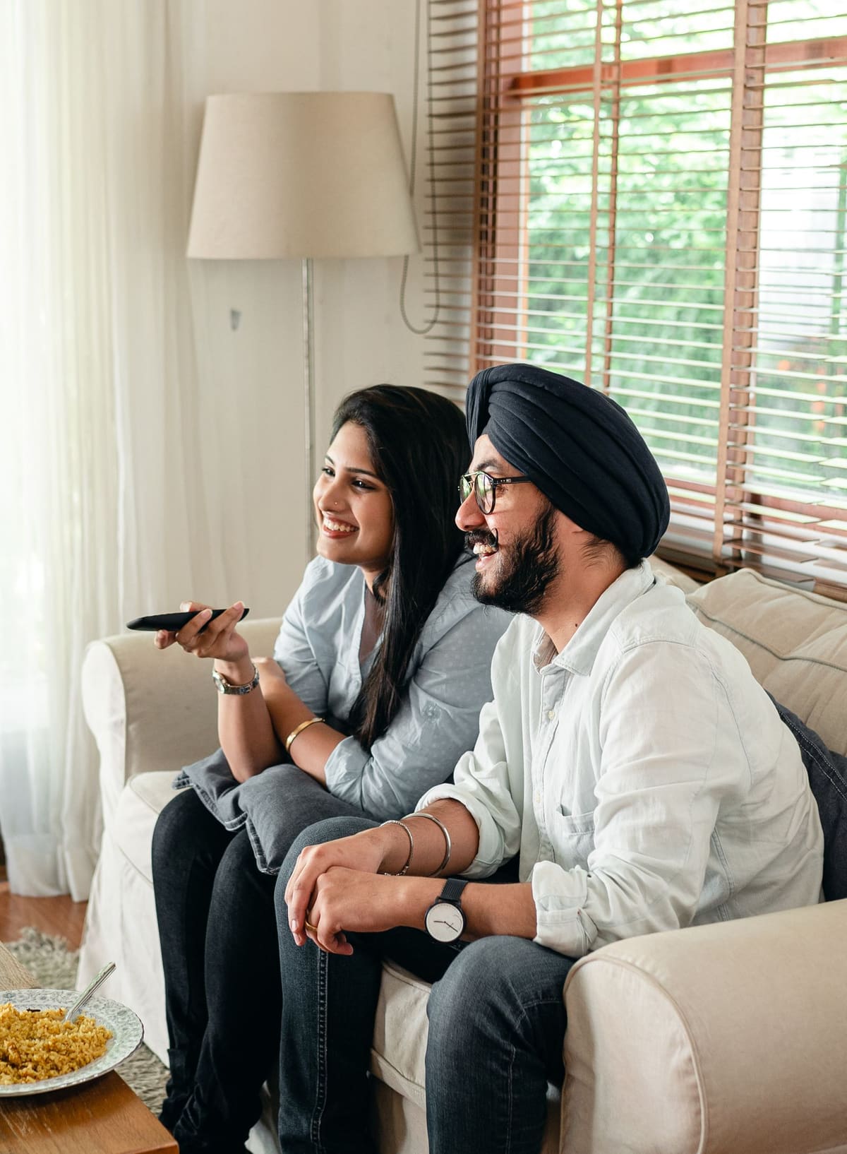 Tersenyum pasangan menonton TV sambil duduk di sofa