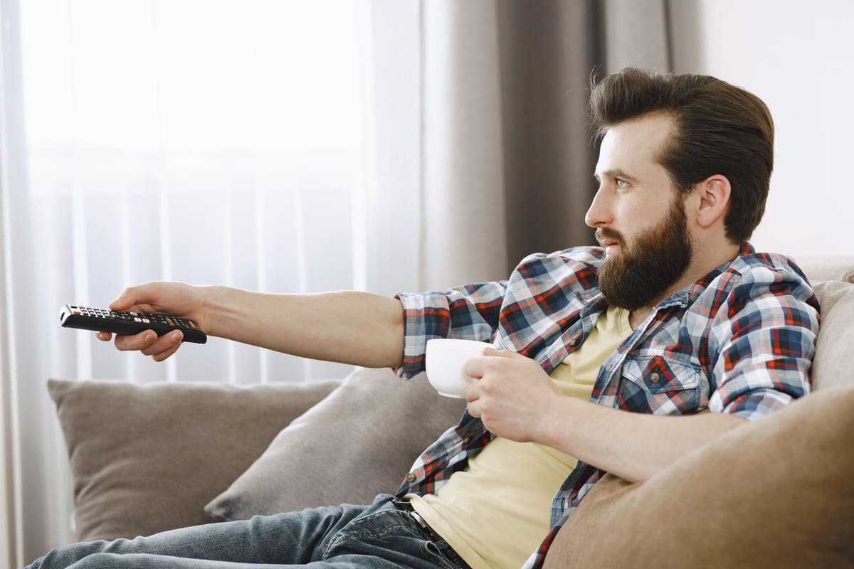 Pria duduk di sofa memegang remote control