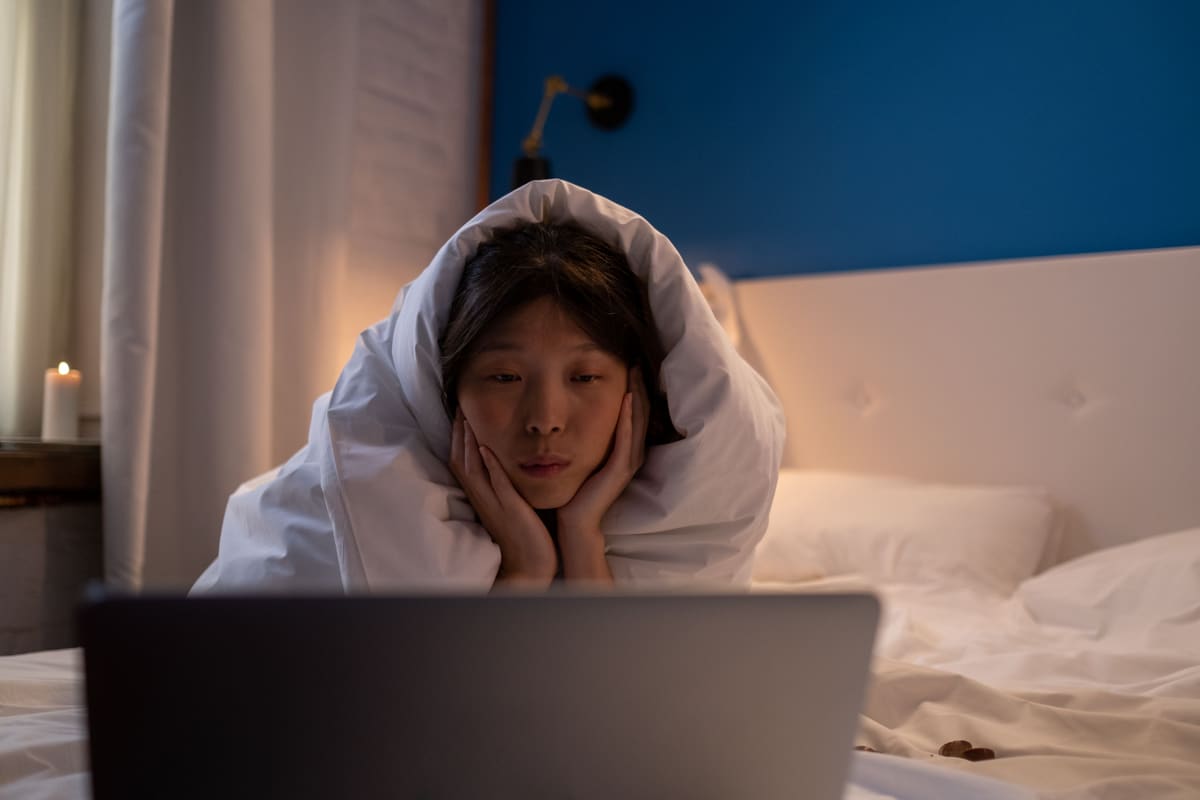 Portrait wanita dengan hands di chin menonton film di laptop